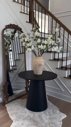 a vase with white flowers sitting on top of a table in front of a staircase