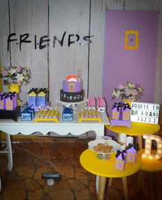 a table topped with cakes and cupcakes on top of yellow stools next to a wall