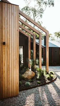 a wooden structure with plants and rocks in the foreground, near a gravel path