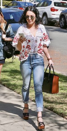 a woman is walking down the sidewalk with her purse and cell phone in hand,