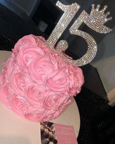 a pink cake decorated with roses and a tiara for the number five on top