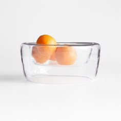 three oranges in a glass bowl on a white surface