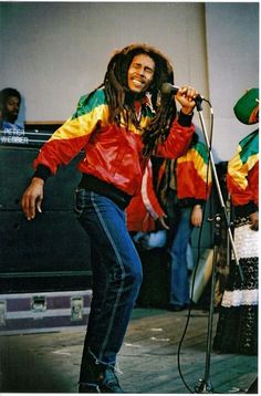 a man with dreadlocks standing in front of a microphone and singing into a mic