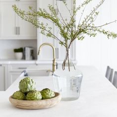 some green vegetables are in a bowl on the kitchen counter next to a glass vase