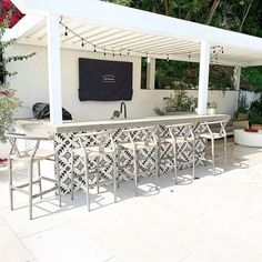 an outdoor bar with chairs and tables under a white pergolan roof, surrounded by greenery