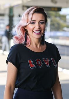 a woman with pink hair wearing a black love t - shirt and large hoop earrings