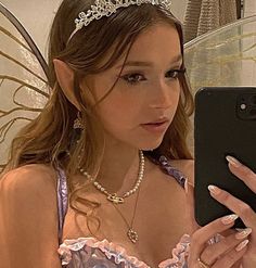 a woman wearing a tiara and holding a cell phone in front of her face