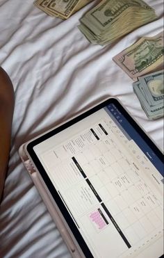 a person laying in bed next to a tablet with money on it