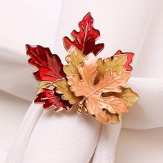 a napkin with a red and gold leaf brooch sitting on it's side