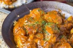 a bowl filled with meat covered in gravy and garnished with parsley