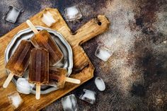 popsicles on a cutting board with ice cubes around them and an empty bowl