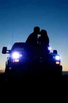 a couple kissing in the bed of a pickup truck at night with lights on it