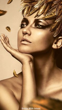 a woman with gold feathers on her head and hands near her face, posing for the camera