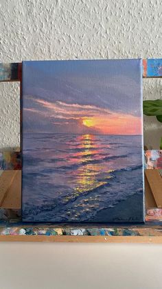 a painting of the sun setting over the ocean on a canvas with paintbrushes