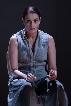 a woman sitting on top of a chair in front of a black background with her hands folded