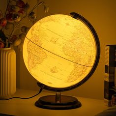 an illuminated globe sitting on top of a table next to a vase with flowers in it