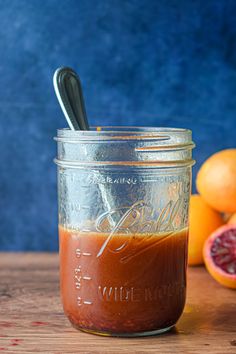 a mason jar filled with liquid next to oranges on a wooden table and blue wall in the background