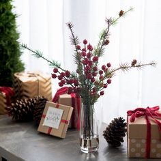 a vase filled with red berries sitting on top of a table next to christmas presents