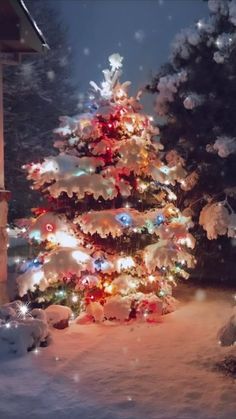 a christmas tree is lit up in the snow at night with colorful lights on it