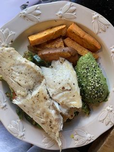 a white plate topped with fish, potatoes and broccoli covered in seasoning