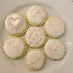 six decorated cookies on a white plate with pink bows and hearts in the shape of heart