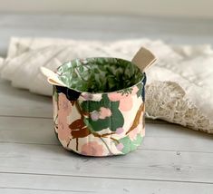 a flowered fabric covered cup with a wooden spoon in it on a white table