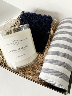 an open box containing a candle, scarf and a striped towel next to a bottle of essentials