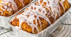 two tins filled with cinnamon rolls covered in icing on top of a cooling rack