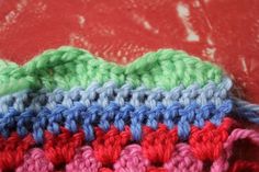 there is a crocheted piece of cloth on the table with red, green and blue yarn