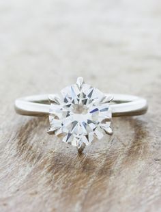 a white diamond ring sitting on top of a piece of wood with the center stone missing