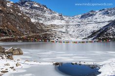 a lake surrounded by snow covered mountains with colorful flags hanging from it's sides