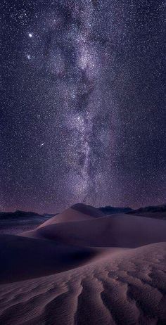 the night sky is filled with stars and clouds above sand dunes in the desert,