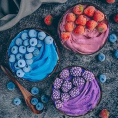 three bowls filled with different types of desserts on top of a stone surface next to strawberries and blueberries