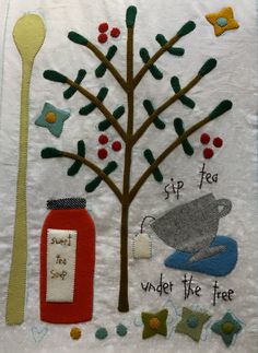 an embroidered wall hanging with spoons, tree, and bottle on it that says under the tree