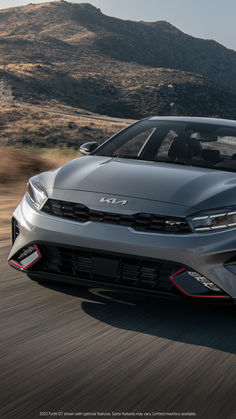 the front end of a silver car driving on a road