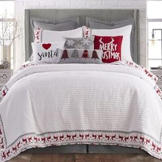 a bed covered in white and red christmas pillows next to a window with snowflakes on it