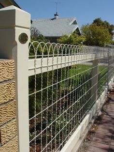 a white fence that is next to a house and some bushes in front of it