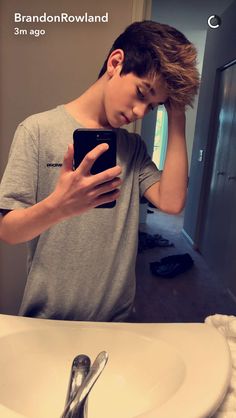 a young man looking at his cell phone in front of a sink with spoons