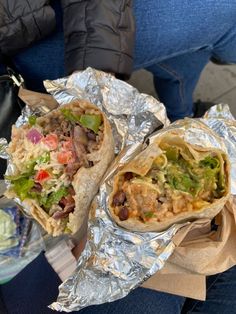 two burritos sitting on top of foil covered in toppings and condiments