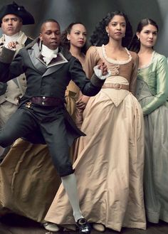 a group of people standing around each other in formal dress and historical clothing, with one man pointing at the camera