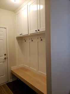 an empty room with white cabinets and wooden bench in front of the door is lit by recessed lighting