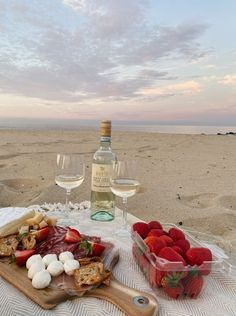 a bottle of wine and some strawberries on a table at the beach with two glasses of wine