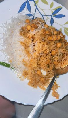 a white plate topped with rice and beans next to a spoon on top of a table