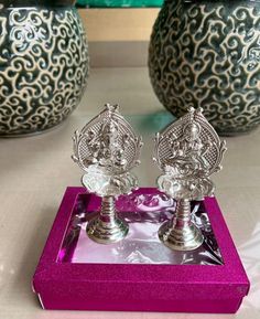 two silver vases sitting on top of a purple box