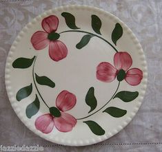 a plate with pink flowers painted on it sitting on a white tablecloth covered table