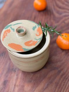 an orange sitting on top of a wooden table next to a jar and two small oranges