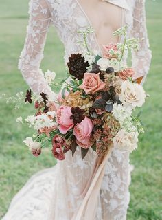 a bride holding a bouquet of flowers in her hands and wearing a wedding dress with long sleeves