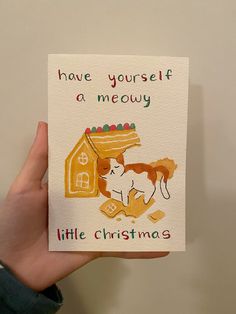 a hand holding up a card with a dog and house on it that says, have yourself a meow little christmas