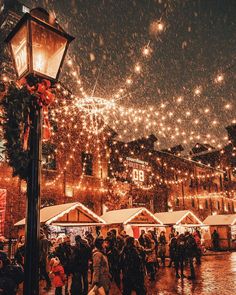 people are walking around in the snow near christmas lights and street lamps on a rainy night