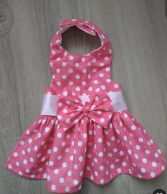 a pink and white polka dot dress with bow on the back, sitting on a wooden floor